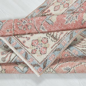 May include: A folded vintage rug with a floral pattern in shades of pink, blue, and white. The rug has a fringed edge and a worn, distressed look.