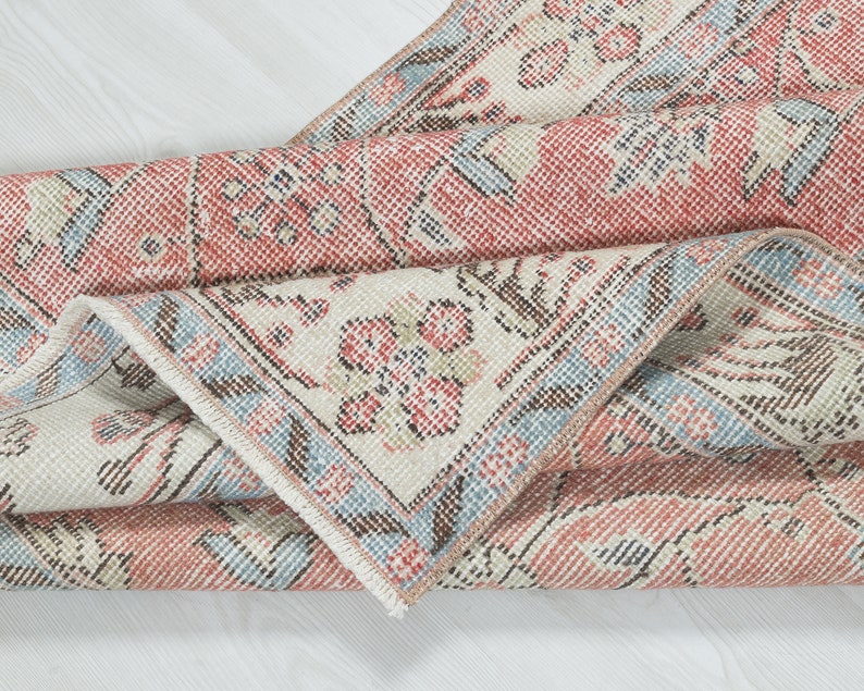 May include: A folded vintage rug with a floral pattern in shades of pink, blue, and white. The rug has a fringed edge and a worn, distressed look.