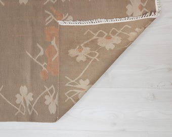 Peut inclure: Un tapis beige à motifs floraux. Le tapis a une bordure en frange blanche et est plié en deux.