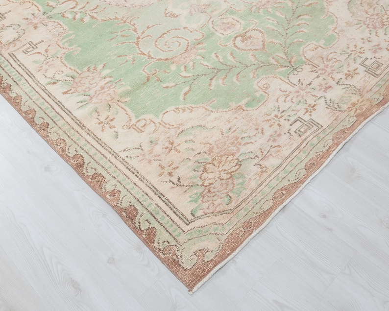 May include: A vintage area rug with a distressed, floral design. The rug features a central field of pale green with floral motifs in shades of pink and beige. The border is a darker brown with a repeating pattern.