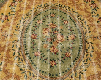 May include: A vintage-style rug with a central oval design featuring a bouquet of yellow and red roses on a green background. The rug has a distressed look with a yellow and brown floral border and a striped pattern.