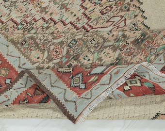 May include: Close-up of a woven rug with a geometric pattern in shades of brown, red, blue, and white. The rug has a fringed edge and is folded in half.