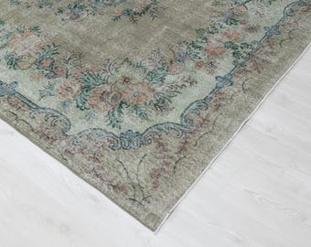 May include: A vintage-style area rug with a faded floral pattern. The rug features a muted color palette of sage green, peach, and blue. The design includes floral motifs and ornate border details, creating a classic and elegant look. The rug is placed on a white wooden floor.