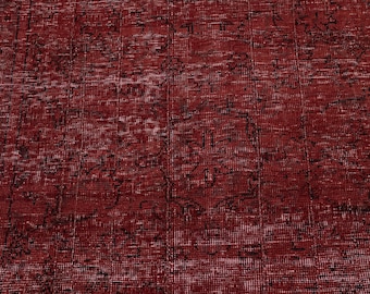 May include: A close-up of a red rug with a distressed, vintage appearance. The rug has a dark red background with black and white accents, creating a textured pattern. The rug's design features faded floral or geometric motifs.