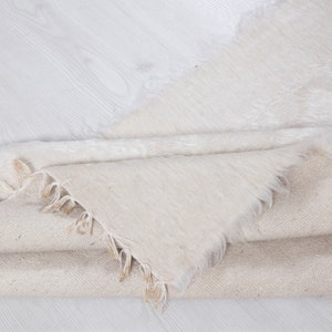 May include: A white, fluffy rug with a frayed edge is folded over a beige fabric. The rug is made of a soft, plush material.
