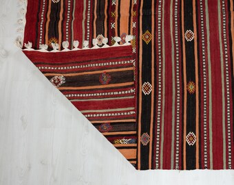 May include: A red, black, and green striped rug with geometric patterns. The rug has fringe along the edges.