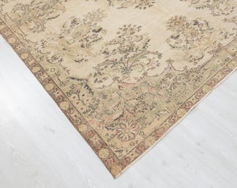 May include: A distressed-look rug with a beige backdrop and detailed floral patterns in brown, green, and pink. The rug features an ornate border. It is placed on a white wooden floor, showcasing its intricate design.