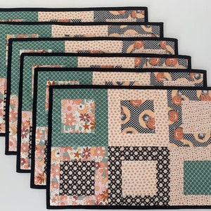 May include: Set of six black-trimmed placemats with a patchwork design featuring floral, geometric, and polka dot patterns in shades of pink, green, and black.