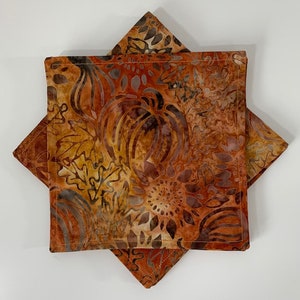 May include: Two brown and orange fabric napkins with a fall-themed pattern of leaves and pumpkins. The napkins are folded in half and stacked on top of each other.