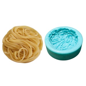 May include: A blue silicone mold shaped like a mound of spaghetti. Next to the mold is a pile of cooked spaghetti.