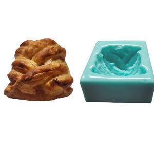 May include: A light blue silicone mold for baking a braided pastry. The mold is empty and the pastry is shown next to it.