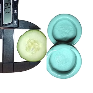 May include: A close-up of a cucumber slice being measured with a digital caliper. The caliper reads 1.79 inches. Two teal-colored silicone molds are shown in the background.