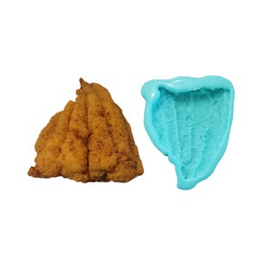 May include: A golden-brown, breaded, triangular-shaped food item with a textured surface next to a matching turquoise silicone mold. The mold features a hollow, ridged interior cavity that mirrors the shape and texture of the food item.