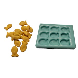 May include: A blue silicone mold with 12 fish-shaped cavities. The mold is designed for baking and creating fish-shaped treats. There are also several yellow fish-shaped crackers scattered around the mold.
