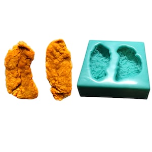 May include: Two orange-colored, fried chicken cutlets next to a teal-colored silicone mold with two cavities shaped like chicken cutlets.