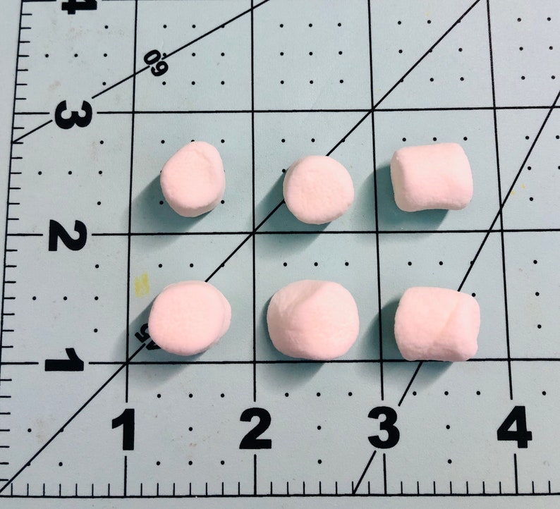 Pu&ograve; includere: Sei piccoli marshmallow cilindrici di colore rosa pallido disposti in due file su un tappetino da taglio azzurro con linee a griglia e numeri neri. I marshmallow sono posizionati contro un righello con misure in pollici, indicando una dimensione di 1,3 cm.