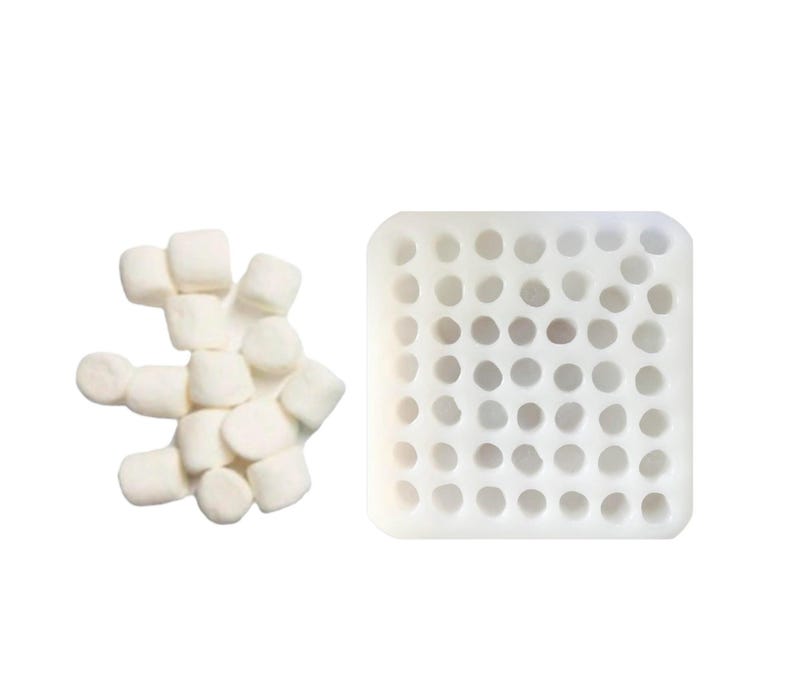 Pu&ograve; includere: Uno stampo in silicone bianco con una griglia di trentasei cavit&agrave; circolari disposte in uno schema quadrato, posizionato accanto a un piccolo mucchio di marshmallow bianchi cilindrici che corrispondono alle dimensioni delle aperture.