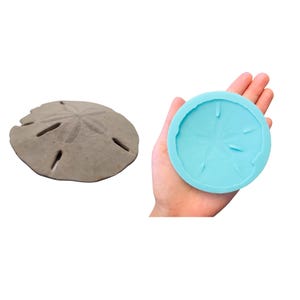 May include: A light blue silicone mold shaped like a sand dollar. The mold is being held in a hand.