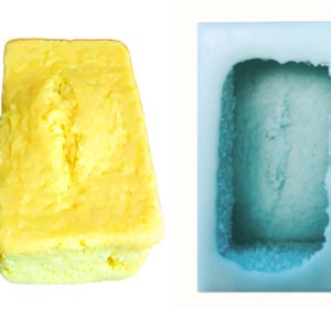 May include: A yellow cake loaf in a blue silicone baking mold. The cake has a crack down the center.