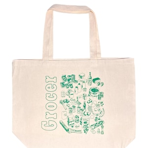Op de afbeelding: Crèmekleurige draagtas met groene illustraties van boodschappen en het woord "Grocer" verticaal afgedrukt. De tas toont een verscheidenheid aan voedingsmiddelen, waaronder fruit, groenten en verpakte goederen.