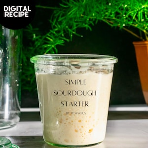 Może przedstawiać: Szklany słoik z białą pokrywką wypełniony bąbelkującym zakwasem chlebowym. Słoik jest oznaczony etykietą "SIMPLE SOURDOUGH STARTER BY POMMUS".