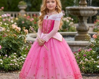 Könnte beinhalten: Ein bodenlanges rosa Kleid mit langen, transparenten Ärmeln, einem weißen schulterfreien Ausschnitt und einem goldverzierten Oberteil mit einem zentralen rosa Schmuckstein. Der Rock aus mehrlagigem Tüll hat goldene Stickereien und einen Spitzenbesatz.