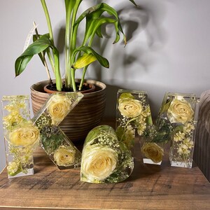 May include: A set of resin letters spelling out the word "MOM" decorated with pressed flowers. The letters are white and feature yellow and white flowers.