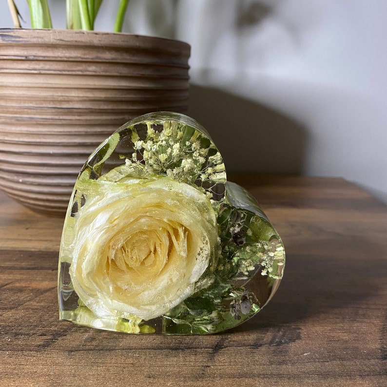 May include: A heart-shaped resin paperweight with a preserved yellow rose and white baby's breath flowers.