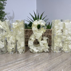 May include: White resin letters spelling "M & H" with dried white flowers embedded in the resin.