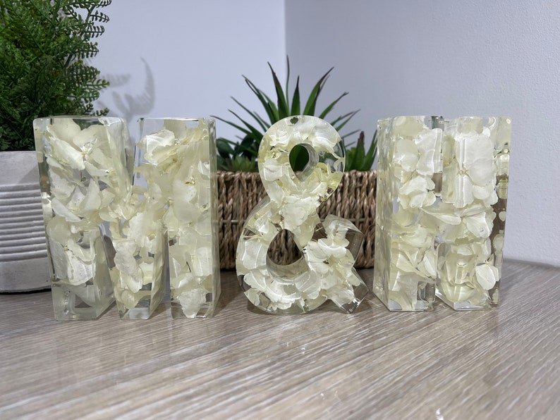 May include: White resin letters spelling "M & H" with dried white flowers embedded in the resin.