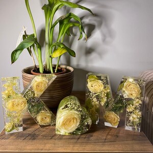 May include: Three resin letters, K, M, and a heart, filled with dried yellow flowers and greenery. The letters are on a wooden surface.