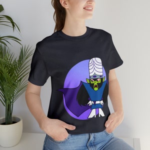 Puede incluir: Camiseta negra con un personaje de dibujos animados que lleva una capa morada y un sombrero blanco con la cara verde. El personaje está delante de un círculo morado y azul.