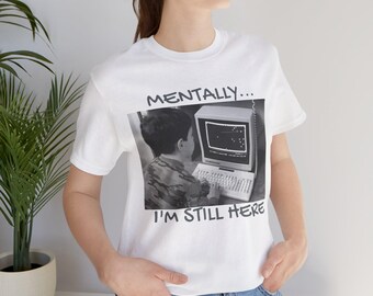 Puede incluir: Camiseta blanca con una imagen en blanco y negro de una persona usando una computadora. El texto en la camiseta dice "Mentally... I'm Still Here."
