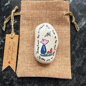 May include: A painted stone featuring a pig illustration and the quote "Sometimes the smallest things take up the most room in our hearts." The stone is in a burlap bag with a tag that says "Handmade with love."