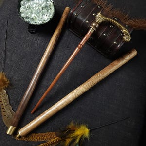 May include: Three wooden walking sticks with different designs. One stick has a brass handle with a decorative design. The sticks are on a dark brown fabric background.