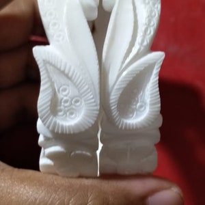 Puede incluir: Un par de piezas decorativas blancas, talladas intrincadamente, con un diseño floral. Las piezas están hechas de un material blanco liso y tienen un aspecto delicado y ornamentado.