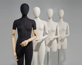 May include: Four mannequins stand in a row, one black and three white. The black mannequin is in the front, with its arms crossed. The white mannequins are behind it, with their arms outstretched.