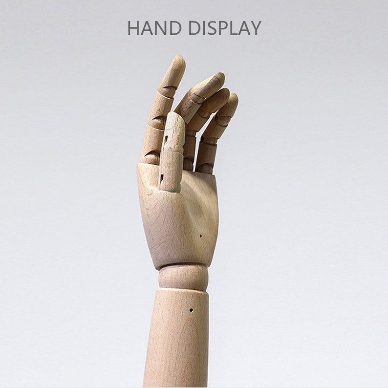 May include: A wooden articulated hand with a natural finish, posed with fingers slightly curved. The text "HAND DISPLAY" is above the hand. This display model is designed for showcasing jewellery, art, or other small items.