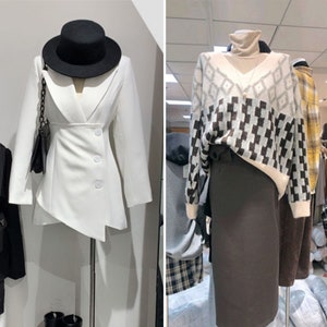 May include: Two mannequins showcase fashion ensembles. One presents a white blazer with an angled hem, complemented by a black hat and handbag. The other displays a patterned sweater over a roll-neck top and a dark brown skirt, offering a contrast in textures and colours.