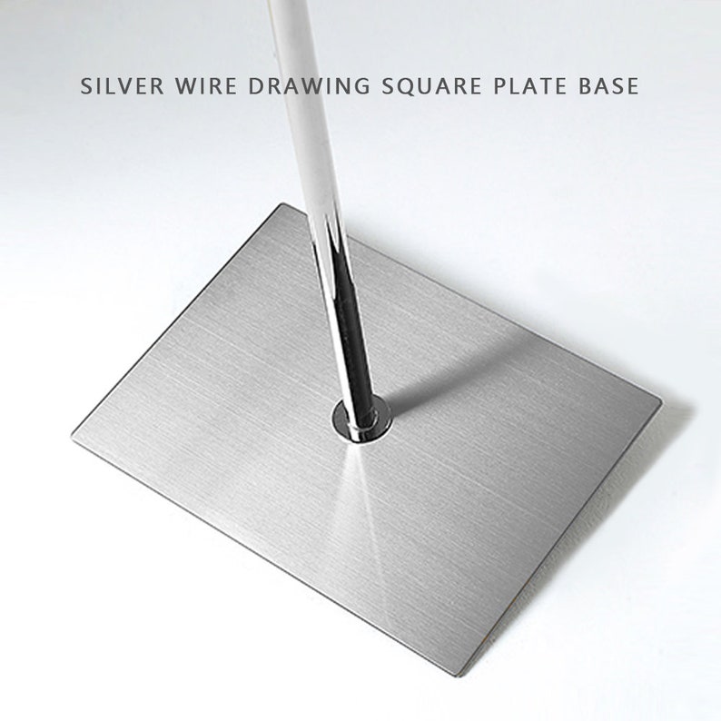May include: A silver metal display stand with a square base and a vertical pole. The base has a brushed metal finish. The text "SILVER WIRE DRAWING SQUARE PLATE BASE" is at the top.