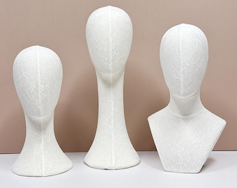 May include: Three white mannequin heads with a delicate floral lace pattern. The heads are in different styles, including a full head, a head with a long neck, and a head with a bust. The heads are displayed on a white surface.