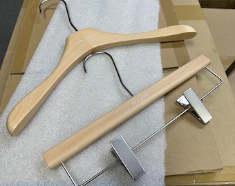 May include: Two wooden clothes hangers with metal hooks and clips. The hangers are light brown with the text "DE-LIANG" printed on them. One hanger is for shirts, and the other is for pants.
