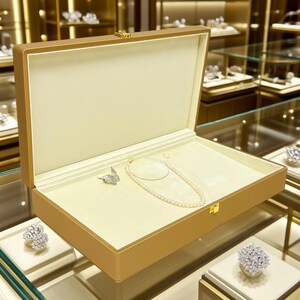 May include: A jewelry display case with a pearl necklace and a butterfly-shaped brooch. The case is open, revealing a cream-colored interior. The case is gold-toned with a gold clasp. Other jewelry pieces are visible in the background.