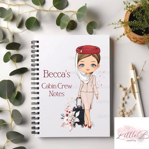 Może przedstawiać: Biały notes w oprawie spiralnej z kreskówkową ilustracją stewardesy w czerwonym kapeluszu i różowym uniformie. Na notesie widnieje napis "Becca's Cabin Crew Notes".