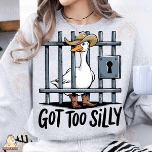 May include: A gray sweatshirt with a white goose wearing a cowboy hat and boots. The goose is behind bars and the text "GOT TOO SILLY" is printed below the image.