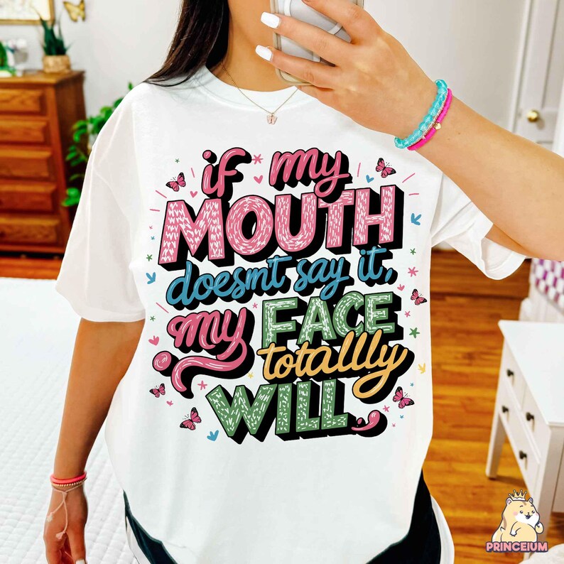 May include: White t-shirt with a colorful graphic that says "If my mouth doesn't say it, my face totally will."