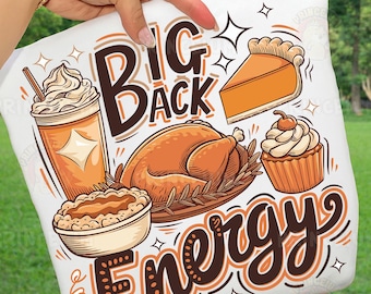 May include: White pillow with a Thanksgiving-themed graphic. The design includes a turkey, pie, cupcake, and a coffee drink. Text reads "Big Back Energy" in brown and orange lettering. The pillow is held up by a person.