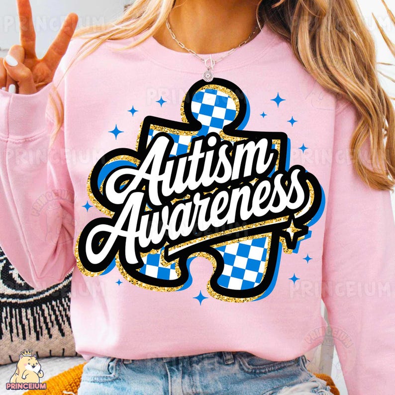 May include: Pink sweatshirt featuring a blue and white chequered jigsaw piece design with the text "Autism Awareness" in gold glitter lettering.