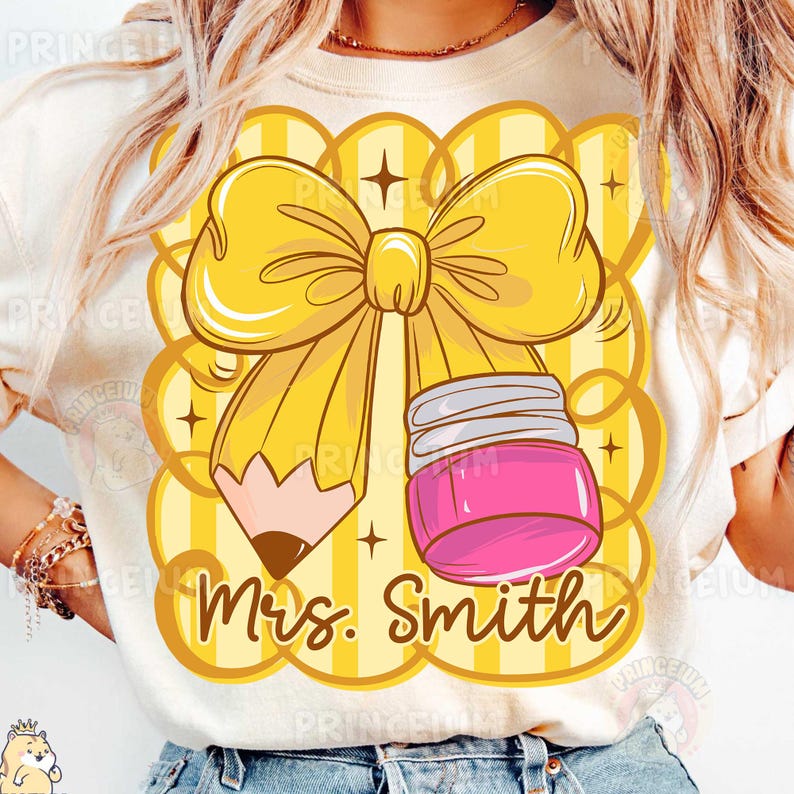 May include: Cream-colored t-shirt featuring a yellow bow, pencil, and pink ink jar design. The design includes the text "Mrs. Smith" in a handwritten style. The background has a yellow scalloped pattern.