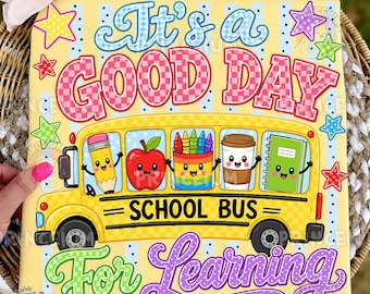 May include: A yellow fabric square featuring a school bus graphic with the text It's a GOOD DAY SCHOOL BUS For Learning. The bus windows display cartoon characters of a pencil, apple, crayons, coffee cup, and notebook, surrounded by stars.